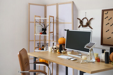 Interior of light office decorated for Halloween with workplace and shelf unit