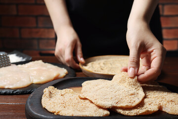 Woman making schnitzel at wooden table, closeup