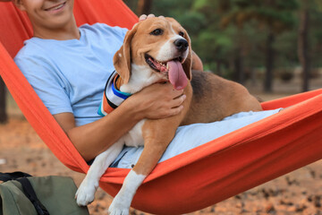 Young man with Beagle dog resting in red hammock outdoors