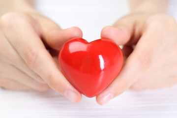 Woman holding red heart at white wooden table, closeup