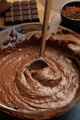 Chocolate dough and spoon in bowl on table, closeup
