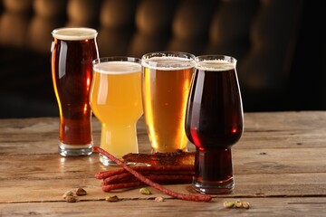 Glasses with different types of beer and snacks on wooden table indoors
