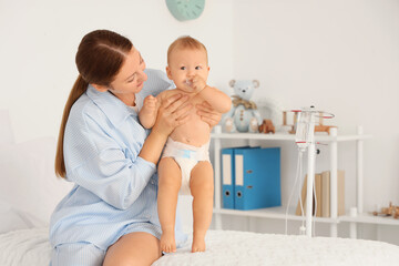 Young mother with her newborn baby sitting on bed in maternity hospital