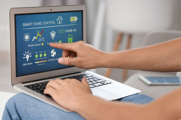 Young man using laptop with smart home application at table in room, closeup