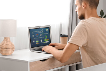 Young man using laptop with smart home application at table in room