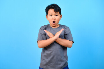 Little boy doing rejection expression, showing crossing arms gesture on blue background