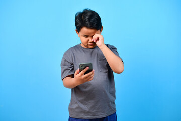 Child boy rubs his eyes for looking at phone. Hyperopia myopia astigmatism glaucoma and addiction...