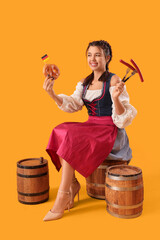 Young Octoberfest waitress with traditional German food sitting on barrel against yellow background