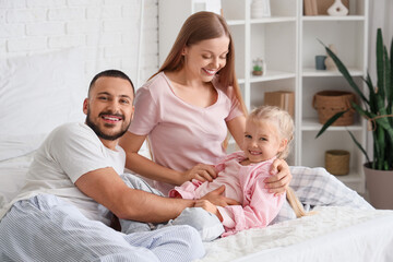 Happy parents tickling their little daughter in bedroom