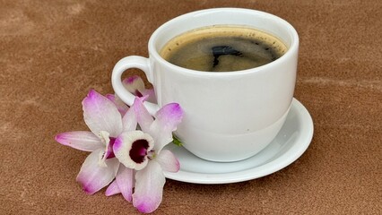 Cup of coffee with pink and white flower on the table. Dendrobium nobile orchid flower, also known as doll's eye. 