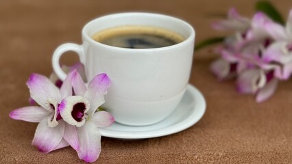 Cup of coffee with pink and white flower on the table. Dendrobium nobile orchid flower, also known as doll's eye. 