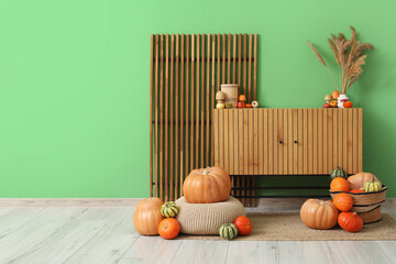 Wooden commode with wicker basket of different pumpkins near green wall at home