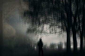 A haunted hooded figure. Standing beneath trees on a spooky winters night in the countryside, With a grunge, historic photo edit
