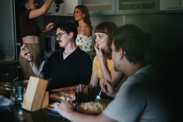 A group of friends having a casual meal in a home kitchen, sharing laughter and enjoying each...