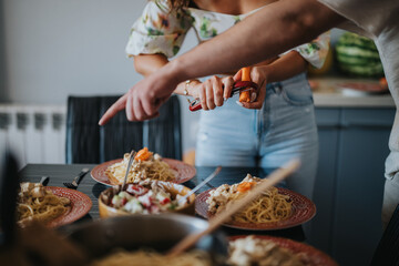 Casual kitchen scene with friends preparing and enjoying a homemade pasta meal. Two people are actively involved in cooking and sharing food, creating a warm and inviting atmosphere.