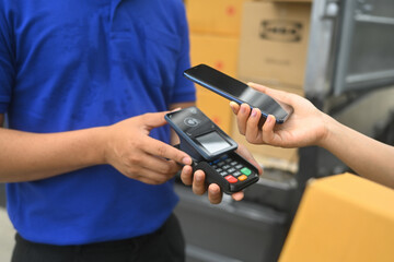Female making a contactless payment with smartphone to delivery man. Digital payments and modern shopping concept