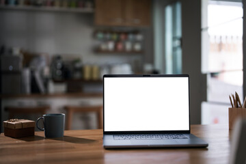 Mockup blank white screen laptop computer on wooden table in home office room.