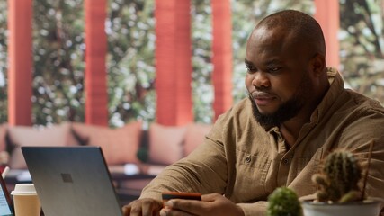 Male freelancer using a card to make an online shopping payment via electronic banking, purchasing to help the startup activity. Small business owner makes a transaction at his home. Camera A.