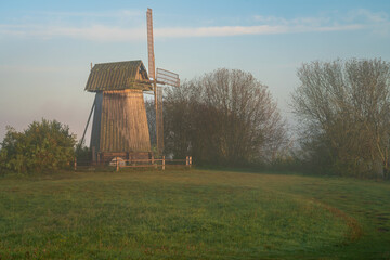 View of an ancient wooden windmill on the banks of the Sorot River on a foggy summer morning,...