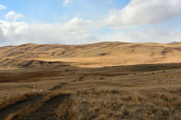 A muddy field road descends into a hilly steppe with dry, yellowed grass on an autumn sunny day.