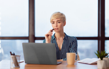 Pensive Female Entrepreneur Thinking Holding Pen Sitting At Laptop Working In Modern Office. Selective Focus