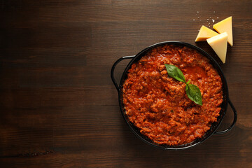 Bolognese sauce in frying pan and pieces of cheese on wooden background, space for text