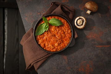 Bolognese sauce in frying pan, mushrooms and towel on dark background, top view