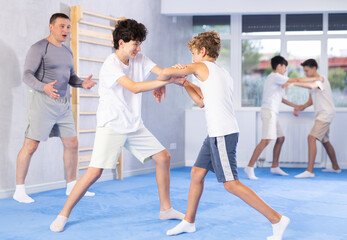 Fototapeta premium Willing junior attendee of self-defense classes fighting with his opponent in sports hall