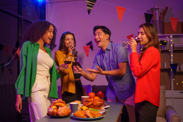 An African American woman and a white woman celebrate with coworkers, drinking, having fun, and smiling together at a lively Halloween night party filled with joy and laughter.