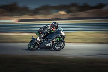  A man rides on a motorcycle's back seat, navigating a winding, lush-green field-lined road