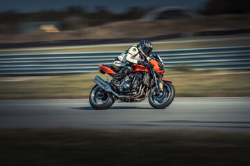  A man rides a red motorcycle along a curvy road, adjacent to a lush green field