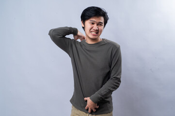 An Asian man appears to be in discomfort, scratching his shoulder with one hand and holding his...