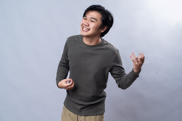 An Asian man mimicking playing a guitar, with his eyes closed and a joyful expression. He is...