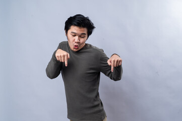 An Asian man with a surprised expression, pointing downward with both index fingers. He is wearing...