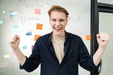 Portrait of happy young businessman wearing blue casual uniform while standing in front of glass board with colorful sticky notes and mind map with confident at creative business meeting. Immaculate.