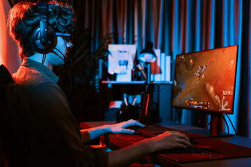 Fototapeta premium Host channel of young gaming streamer playing fighting Moba at battle arena game with multiplays team, wearing headphone on pc monitor with back side image at neon digital light modern room. Gusher.