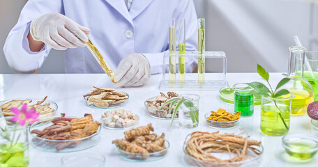 A scientist wearing lab coat and gloves is holding and examining a test tube filled with a yellow...