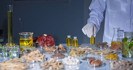 Modern lab setting with gray background features a scientist carefully picks up a vial containing a yellow liquid. The lab table is filled with various herbs, roots, and lab equipment.