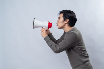 An Asian man in a gray long-sleeve shirt holds a megaphone, expressing a fierce or intense look. He is standing against a plain white background