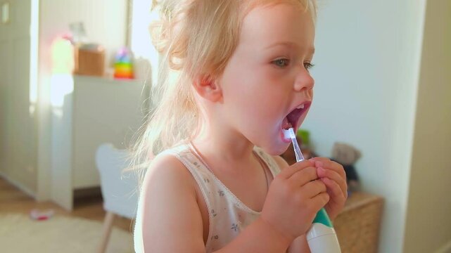 Caucasian cute kid toddler girl brushing her teeth with an electronic toothbrush.