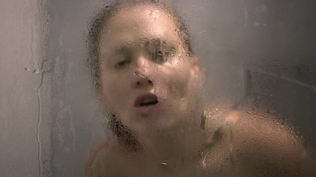 Young sexy woman in shower. Woman in bathroom kissing and touching her lips to misted shower glass