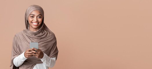 Modern Communication Concept. Portrait Of Cheerful Afro Muslim Girl In Hijab With Smartphone In Hands Looking At Camera, Yellow Background, Copy Space