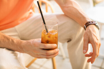 Close-up of a young man in light trousers drinking iced bumble coffee on the terrace of a cafe on a sunny summer day.