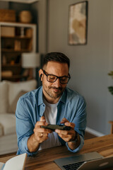Excited Man Using Smartphone for mobile shopping while Sitting in Living Room. Happy Man buying things, shopping online, using a mobile app