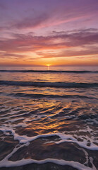 Obraz premium A serene sunset over a calm ocean, with soft waves gently lapping the shore, and the sky transitioning from warm oranges and pinks to deep purples.