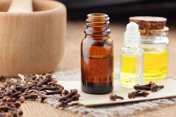 Cloves essential oil or extract in glass bottle with  spice buds on wooden table, closeup, natural medicine and healthy skin and body treatment concept