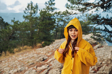 A fearless woman in a vibrant yellow raincoat conquering the heights of a lush mountain landscape