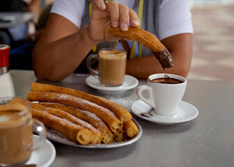 Woman keep pies of  churros in hear hand. Churros popular delicious spanish food with hot chocolate, sugar and coffe on restaurant table