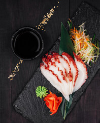 Sliced octopus sashimi with soy sauce and wasabi on slate serving board