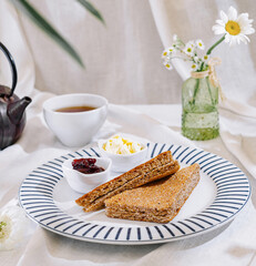 Two slices of toasted bread with butter and jam on a table with tea and flowers